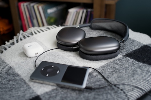 A photograph of my AirPods Max in Space Gray, plugged into an iPod Video with an AirPods Pro 2 to the side. They're all laid haphazardly on a checked wool blanket.